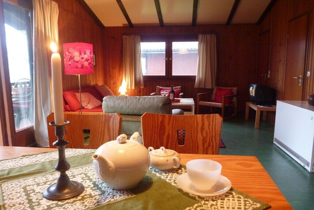 A cozy room with a wooden interior, a table set with a teapot, cups, and a candle, and a television on a wooden cabinet.
