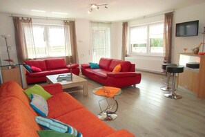 Una sala de estar con sofás rojos, una mesa de centro y un televisor montado en la pared.