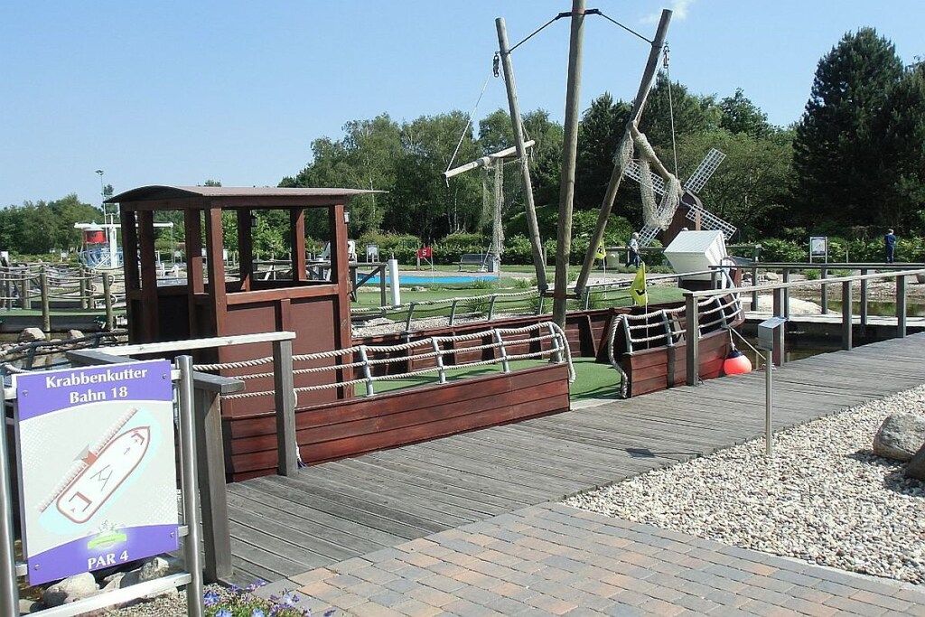 A wooden boat model with a small cabin, a rope barrier, and a sign indicating 'Krabbenkutter Bahn 18 PAR 4'.