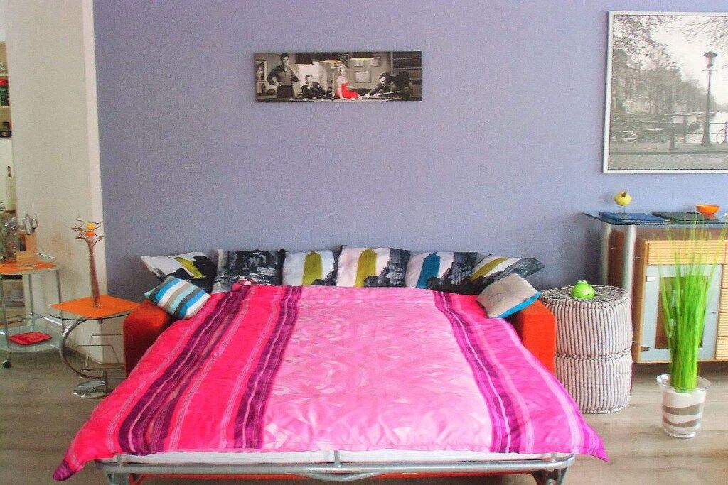 A room with a bed, a chair, a small table, and a picture on the wall.