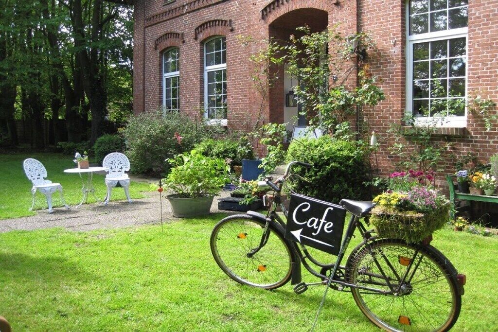 Una bicicleta con una cesta de flores estacionada frente a un edificio de ladrillo con letrero de cafetería.
