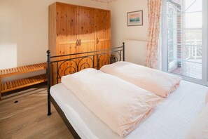 A bedroom with a bed, wooden wardrobe, and a window with curtains. - Holiday apartment in Juist with swimming pool (Juist)