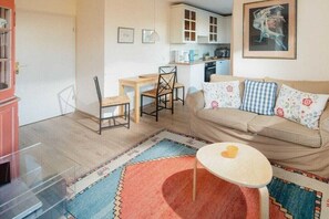 A compact living space with a kitchenette, a dining area, and a sofa with patterned cushions. - Holiday apartment in Juist with swimming pool (Juist)