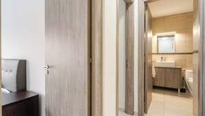Een hotelkamer met een houten deur, een bed met hoofdeinde en uitzicht op de badkamer met een wastafel en spiegel.