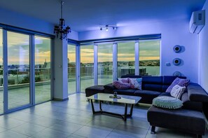 Ein modernes Wohnzimmer mit einem schwarzen Sofa, einem Couchtisch und Blick auf die Stadt durch große Glasfenster.
