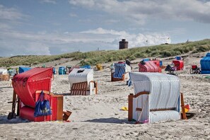 Strandstühle und Sonnenschirme an einem Sandstrand mit Dünen im Hintergrund.