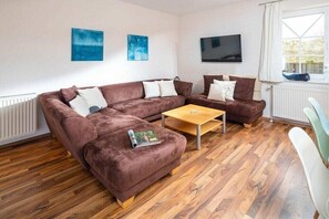Ein Wohnzimmer mit einem braunen Sofagarnitur, einem Holztisch und einem an der Wand befestigten Fernseher.