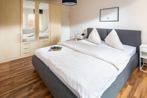 Ein Schlafzimmer mit einem Bett, einem Kleiderschrank, einem Nachttisch und einem gerahmten Bild an der Wand.