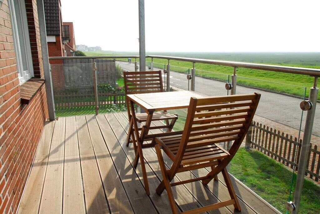Eine Holzterrasse mit Tisch und Stühlen, mit Blick auf eine Straße und eine grüne Landschaft.