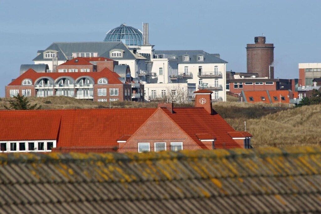 En kystbygning med flere røde tage, en stor hvid bygning med en kuppel og et tårn med et ur.