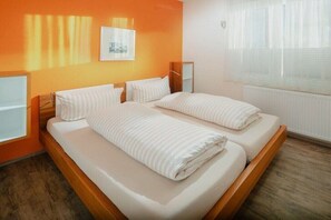 A double bed with white bedding in a room with orange walls and a window with blinds. - Holiday apartment in Juist with swimming pool (Juist)