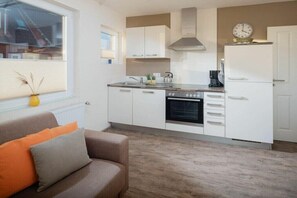 A compact kitchen with white cabinets, a stove, and a clock on the wall. - Holiday apartment in Juist with swimming pool (Juist)