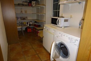 A laundry area with a washing machine, a microwave, and shelves with various items. - in the middle of an organic fruit farm (Elbinsel Krautsand)