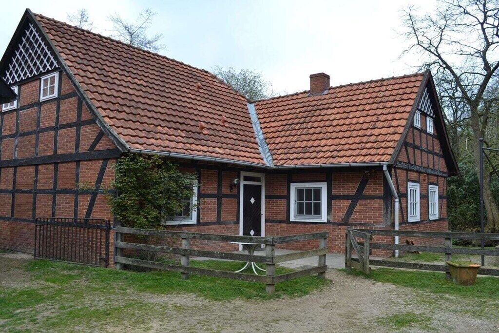 Een traditioneel vakwerkhuis met een steile, puntige kap, een houten hek en een grindpad.