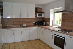 A kitchen with white cabinets, a microwave, a coffee maker, and a stove. - Guesthouse with 4 bedrooms (Berge OT Börstel)