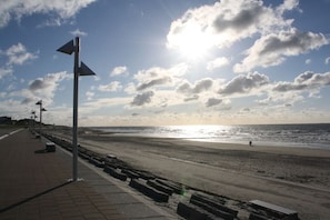 Ein Strand mit gepflastertem Gehweg, Bänken und blauem Himmel mit Wolken.