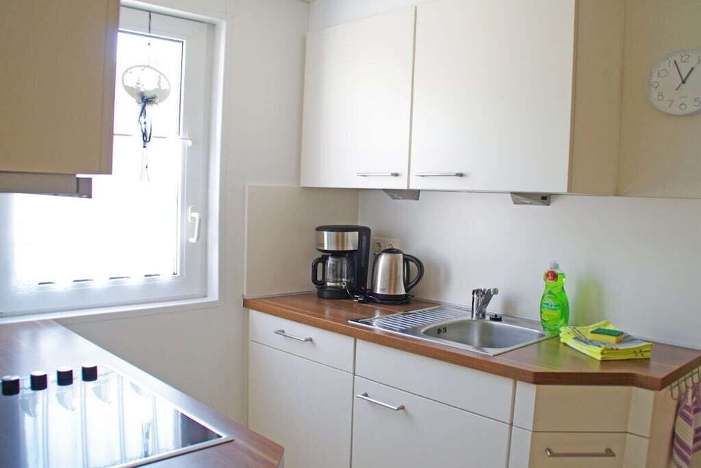 Una cucina compatta con una finestra, una macchina da caffè, un lavandino e una sveglia appesa al muro.