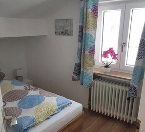 A bedroom with a bed, a radiator, a window with curtains, and a potted plant. - Holiday apartment in Wallgau with Wi-Fi (Wallgau)