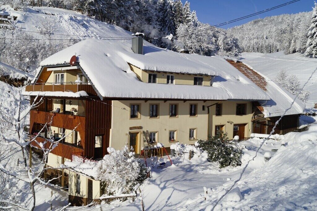 A multi-story building with a sloped roof, surrounded by snow-covered trees and a clear sky.