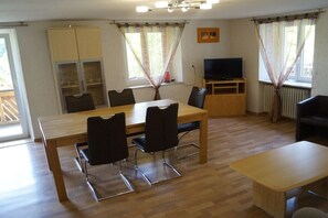 Un coin repas avec une table et des chaises en bois, un téléviseur posé sur un meuble et un buffet aux portes vitrées.