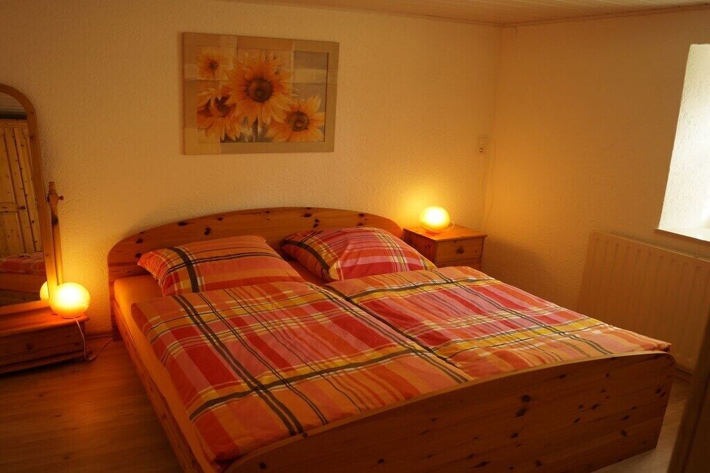 A bedroom with a wooden bed, two bedside lamps, a wall-mounted painting, and a window with blinds.