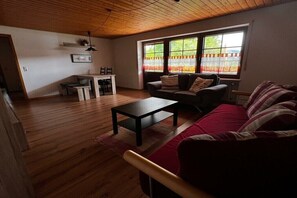 Ein Wohnzimmer mit Holzboden, einer Couch, einem Couchtisch und einem Essbereich mit Tisch und Stühlen.
