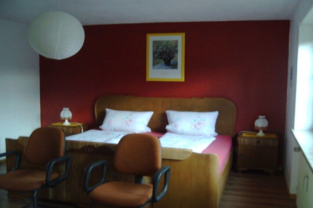 Ein Schlafzimmer mit einem Bett, zwei Nachttischen, einem Sessel und einer Pendelleuchte.