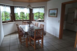 A dining area with a table set for six, wooden chairs, a vase with dried flowers, and a view of greenery through the windows. - Holiday apartment with 1 bedroom (Kleines Wiesental - Sallneck)