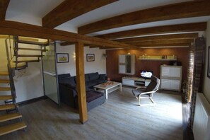 Ett kompakt bostadsutrymme med en trappa, en soffa, ett litet matbord, ett köksområde och en tv.