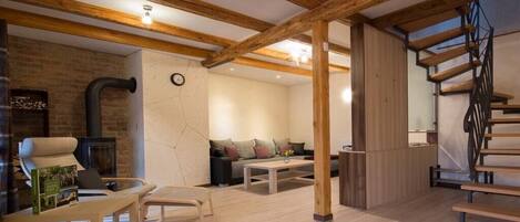 A spacious living area with exposed wooden beams, a brick fireplace, a sofa set, and a staircase.