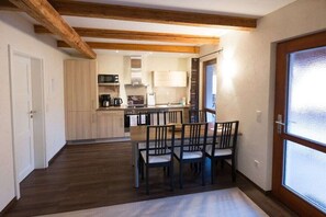 A modern kitchen with wooden beams, a dining area with chairs, and a large window. - To the adventure forge (Kammerforst)