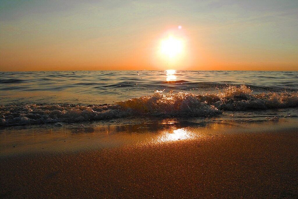 Ein Strandbild, bei dem die Sonne über dem Wasser untergeht und eine ruhige Atmosphäre schafft.