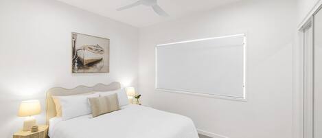 A bedroom with a bed, bedside lamps, a ceiling fan, a painting, and a window.