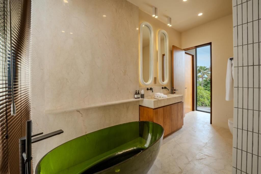A modern bathroom with a green bathtub, a vanity with a mirror, and a view of the outdoors.