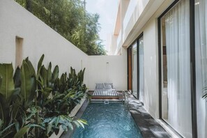 Una piscina con un banco, rodeada de plantas y un edificio con ventanas grandes.
