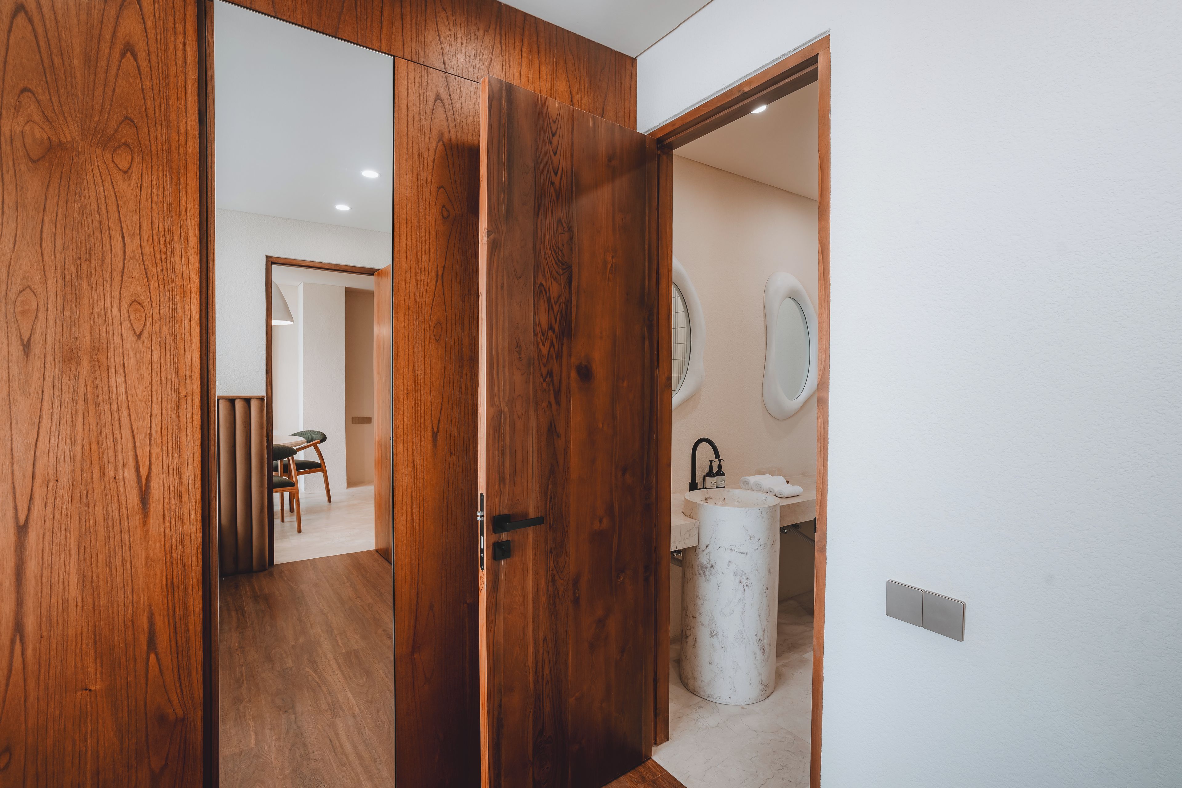 Puerta de madera que da a un baño con un lavamanos y un espejo.