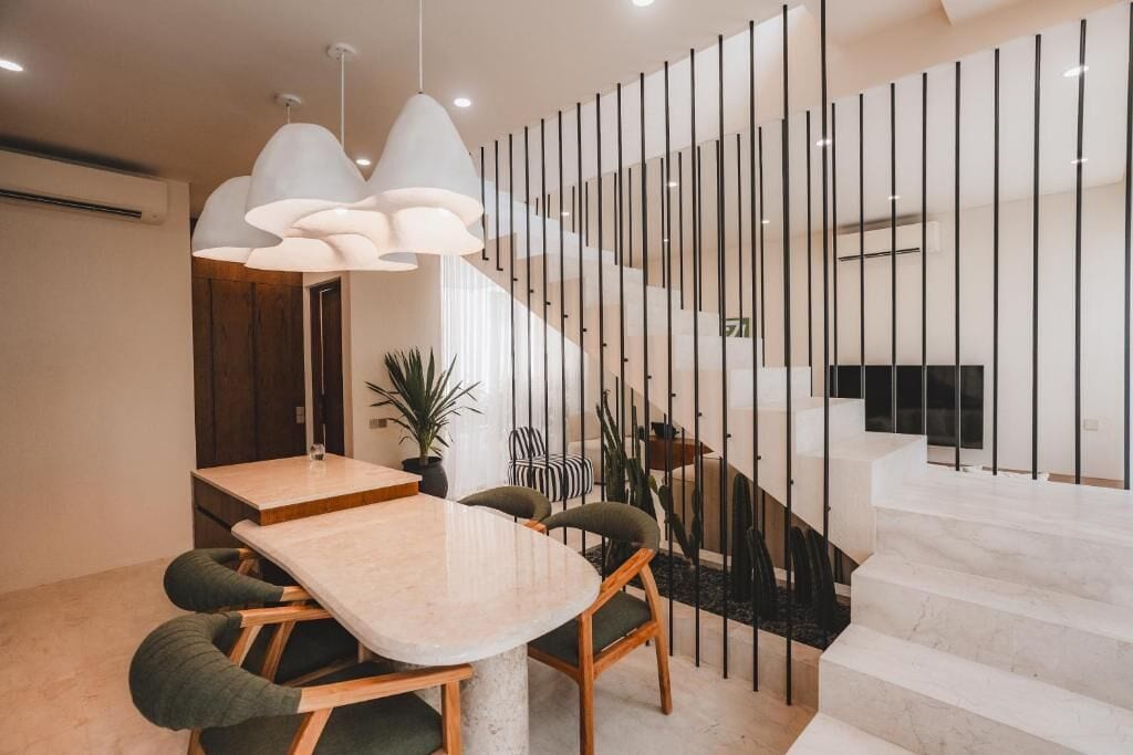 A modern dining area with a marble table, green upholstered chairs, and pendant lighting.
