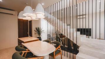 A modern dining area with a marble table, green upholstered chairs, and pendant lighting.