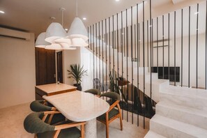 A modern dining area with a marble table, green upholstered chairs, and pendant lighting. - SUOM Apartments & Villas Berawa Canggu (Badung)
