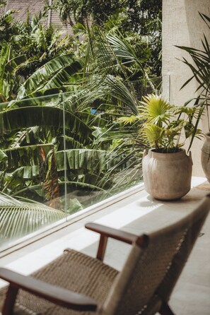 Una habitación con un ventanal grande que da a un jardín exuberante con diversas plantas y una hamaca.