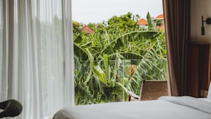 Une chambre d’hôtel avec un lit, une chaise et une vue sur une végétation luxuriante et les bâtiments environnants.