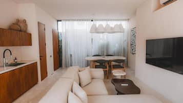 A modern living room with a sofa, a coffee table, a TV, and a dining area with a table and chairs.