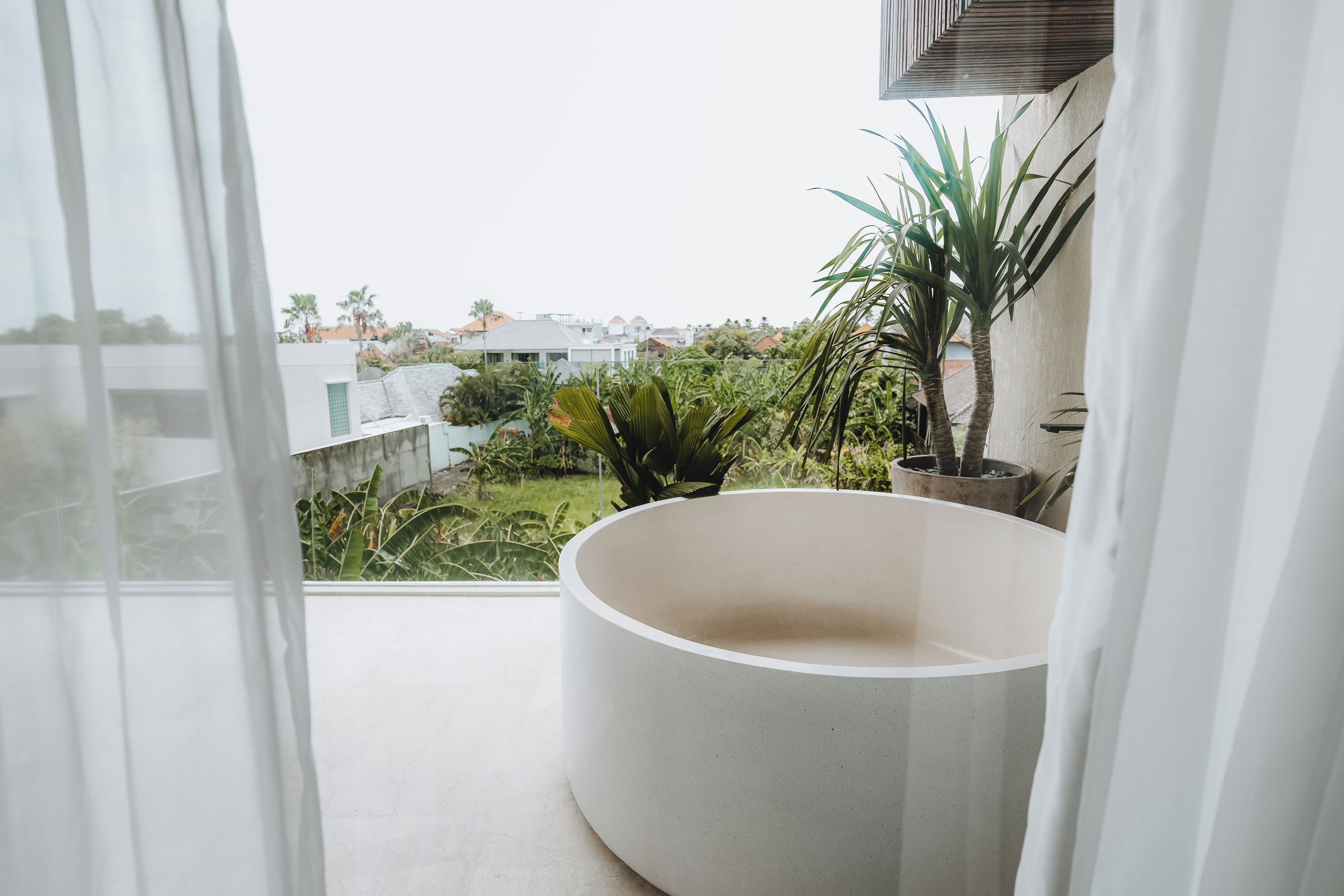 A balcony with a large white bathtub, potted plants, and a view of a residential area.