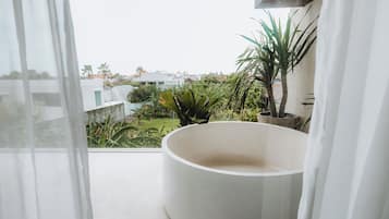 Un balcón con una bañera blanca grande, plantas en macetas y vistas a una zona residencial.