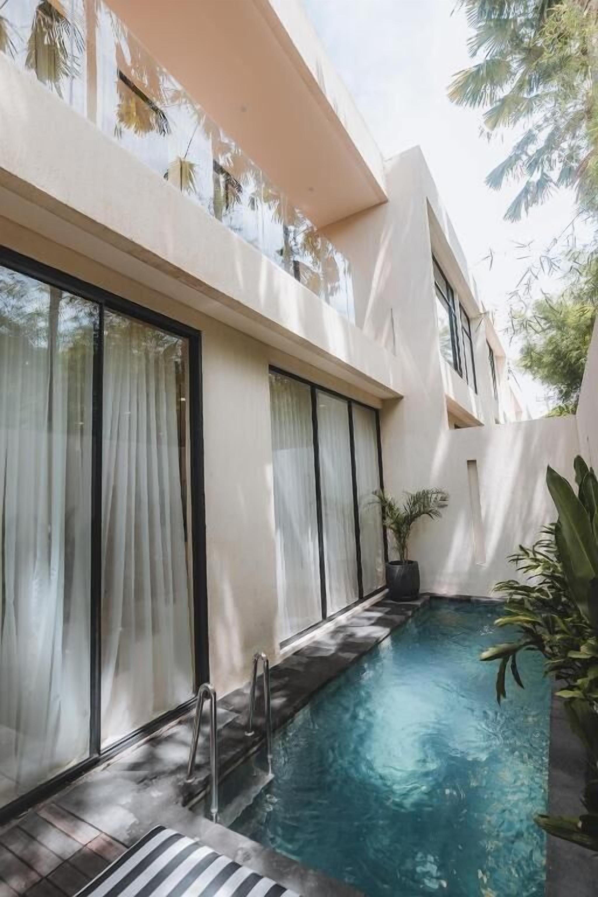 A swimming pool with a glass enclosure, a metal ladder, and a potted plant.