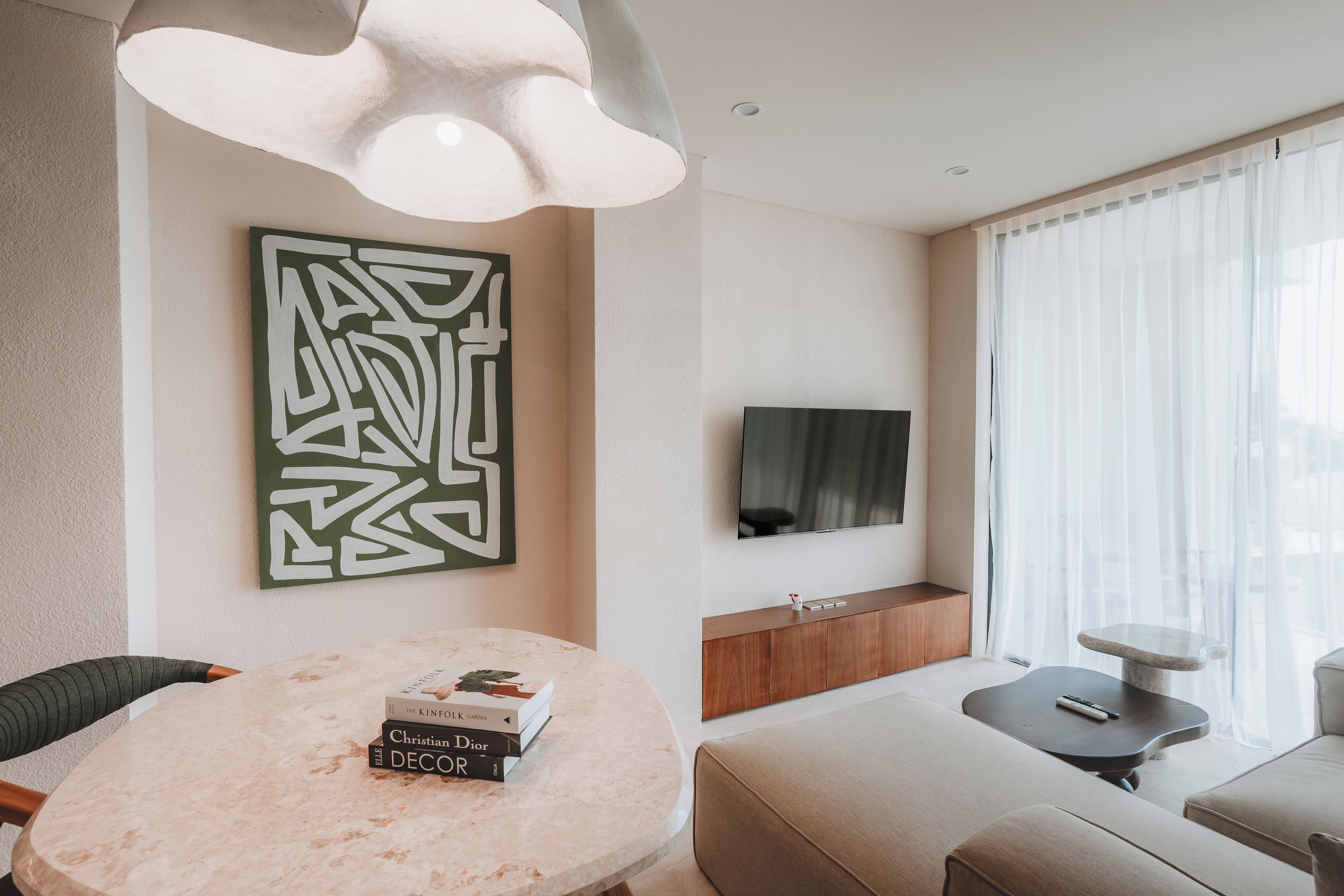 A modern living room with a round marble table, a mounted TV, and a large abstract artwork on the wall.