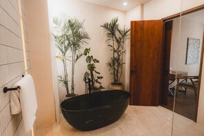Un baño con una bañera negra, plantas en macetas, una puerta de madera y un perchero para toallas.