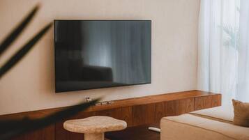 Un soggiorno moderno con una TV a schermo piatto montata a parete, un mobiletto in legno sottostante, uno sgabello rotondo e un divano beige.