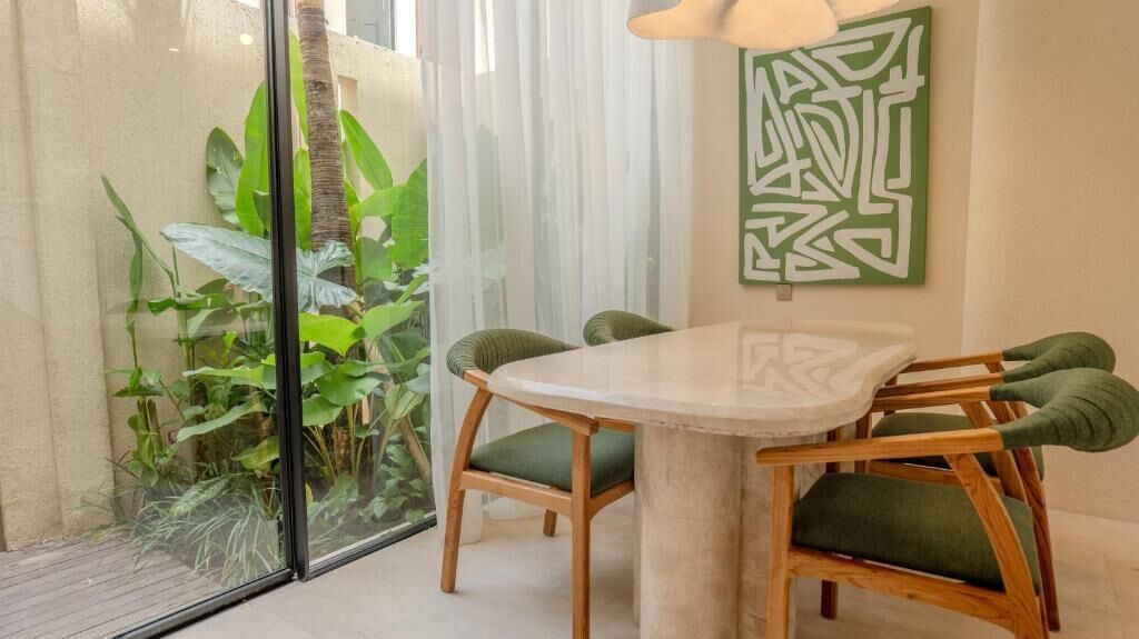 A dining area with a round table and chairs, a glass partition, and a green abstract painting on the wall.