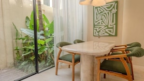 Un espace repas comprenant une table ronde et des chaises, une cloison en verre et un tableau abstrait vert accroché au mur.
